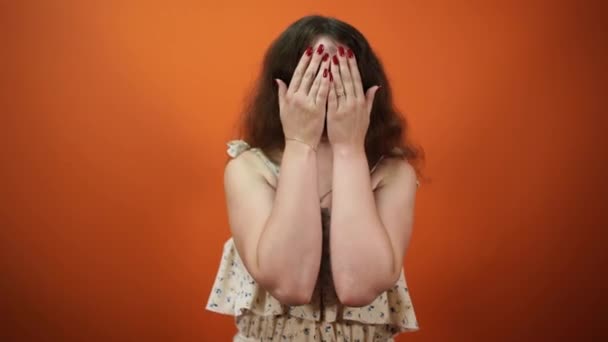 Vista de cerca de la mujer alegre abrir su cara mientras muestra muecas sobre fondo naranja — Vídeos de Stock
