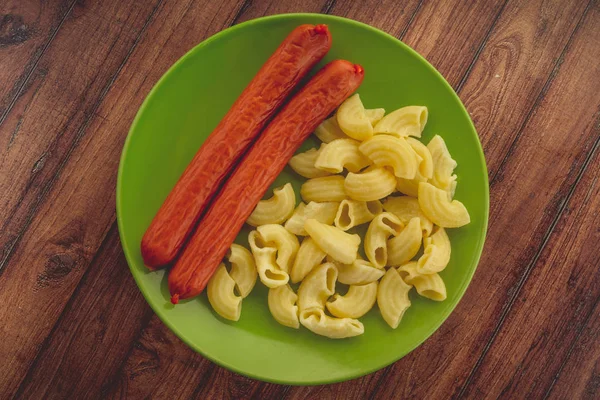 Pasta y salchichas en un plato verde sobre una mesa de madera. pasta en primer plano — Foto de Stock