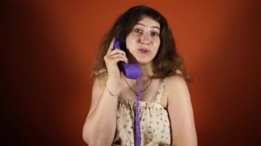 Turuncu bir arka planüzerinde telefonda konuşan bir kadın. Kadın telefon alıcısını, sabit telefonu tutuyor. Sabit hatta konuşan kadın