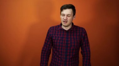 Erkek hapşırık. Adam elinin arkasında hapşırır, turuncu bir arka plan üzerinde duruyor. Konsept: soğuk ve burun akıntısı