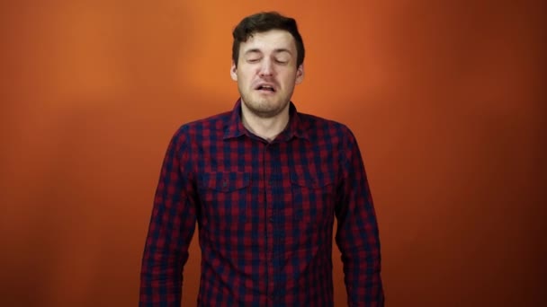 Estornudos masculinos. El hombre estornuda detrás de su mano, de pie sobre un fondo naranja. Concepto: nariz fría y líquida — Vídeos de Stock