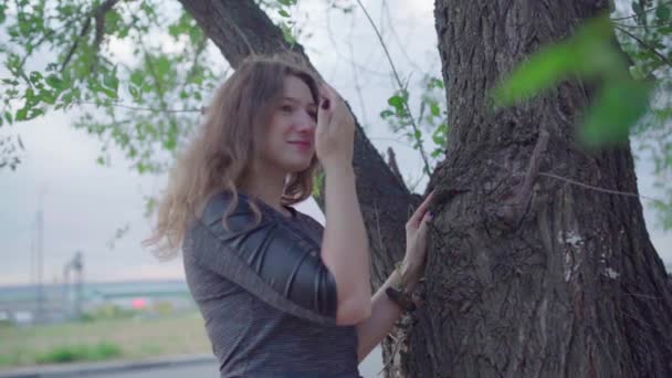 Жінка позує стоячи поруч з деревом, похмурий день — стокове відео