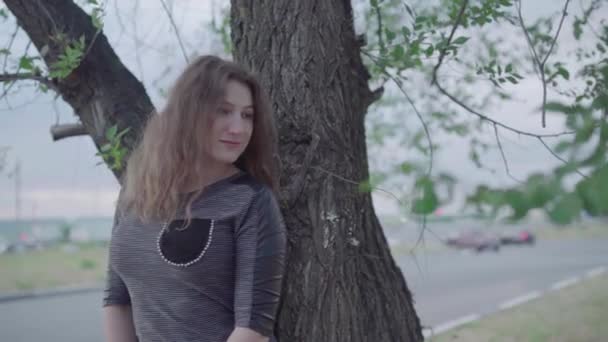 Mujer posando de pie junto a un árbol, día nublado — Vídeos de Stock