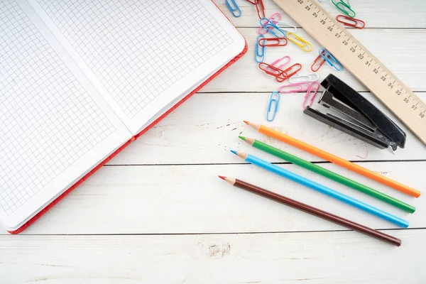 Diverse briefpapier geplaatst op timmerhout tafel. Van boven gekleurde potloden en open notebook gerangschikt op houten tafel in de buurt van paperclips en nietmachine met liniaal voor studies — Stockfoto