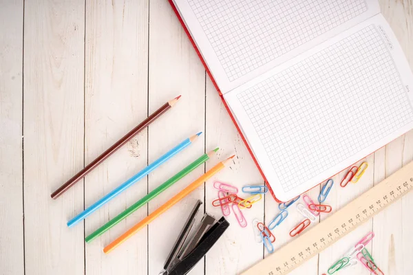 Diverse briefpapier geplaatst op timmerhout tafel. Van boven gekleurde potloden en open notebook gerangschikt op houten tafel in de buurt van paperclips en nietmachine met liniaal voor studies — Stockfoto