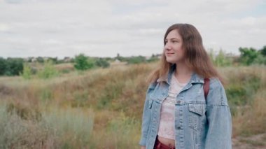 Genç kadın doğanın arka planına karşı mesafe içine bakıyor. Sevimli gülümseyen kadın açık havada ayakta.