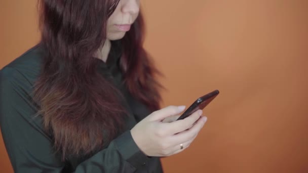 Mujer joven sosteniendo el teléfono móvil en la mano sobre fondo naranja. Mujer escribiendo un mensaje en un teléfono inteligente — Vídeo de stock