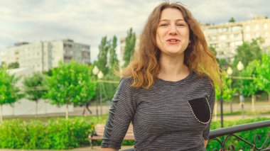 Süslü demir çitlere karşı yeşil parkta duran mutlu kadın. Utangaç kadın bahçede el ele tutuşuyor.