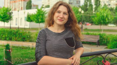 Süslü demir çitlere karşı yeşil parkta duran mutlu kadın. Utangaç kadın bahçede el ele tutuşuyor.