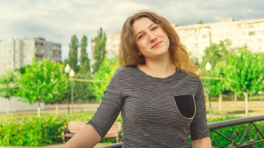 Süslü demir çitlere karşı yeşil parkta duran mutlu kadın. Utangaç kadın bahçede el ele tutuşuyor.