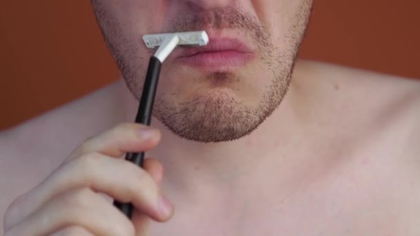 Attraktiver Mann mit blauem Rasiermesser in den Händen rasiert sich die Haare mit vereinzelten Achseln auf orangefarbenem Hintergrund — Stockvideo