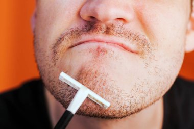 Elinde mavi jilet olan çekici bir adam turuncu arka planda izole edilmiş koltukaltları olan kıllarını tıraş edecek.