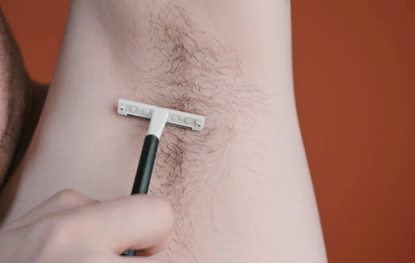 Attractive man with a blue razor in his hands is going to shave hair with armpits isolated on orange background — Stock Photo, Image