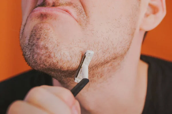 Aantrekkelijke man met een blauw scheermes in zijn handen gaat haar scheren met oksels geïsoleerd op oranje achtergrond — Stockfoto