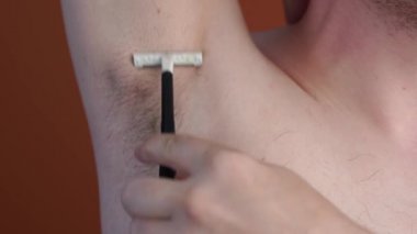 Elinde mavi jilet olan çekici bir adam turuncu arka planda izole edilmiş koltukaltları olan kıllarını tıraş edecek.