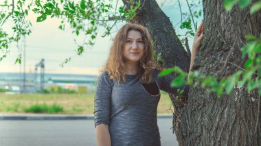 Ağacın yanında durup kameraya bakan güzel bir kadın.