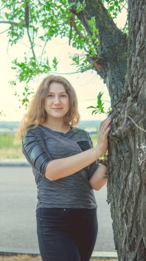 Ağacın yanında durup kameraya bakan güzel bir kadın.