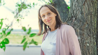 Ağacın yanında durup kameraya bakan güzel bir kadın.