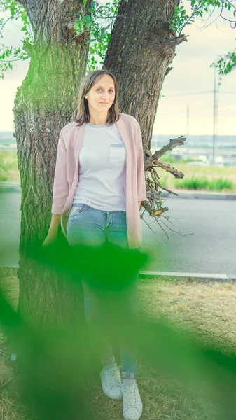 Mulher bonita de pé perto de uma árvore e olhando para a câmera — Fotografia de Stock