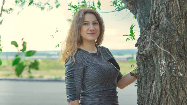 Hermosa mujer de pie cerca de un árbol y mirando a la cámara — Foto de Stock