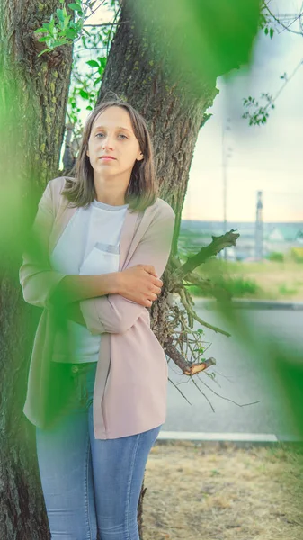 Gyönyörű nő áll egy fa mellett, és a kamerába néz. — Stock Fotó