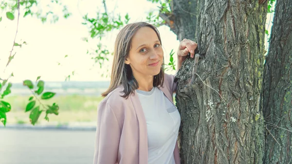 Ağacın yanında durup kameraya bakan güzel bir kadın.