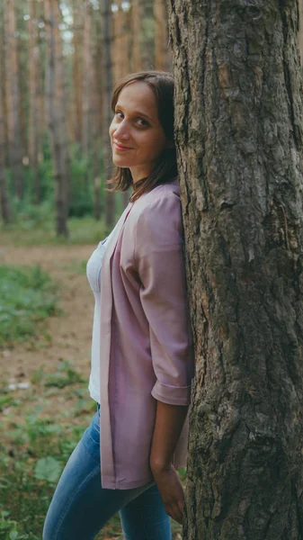 Serieuze vrouw kijkt uit van achter de boom. Mooie rustige vrouw aanraken boom en kijken naar camera in rustig bos — Stockfoto