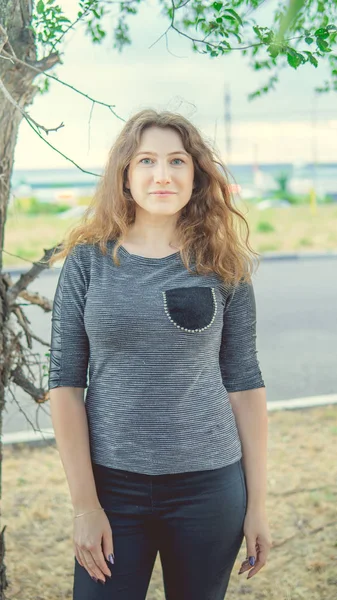 Hermosa mujer de pie cerca de un árbol y mirando a la cámara — Foto de Stock