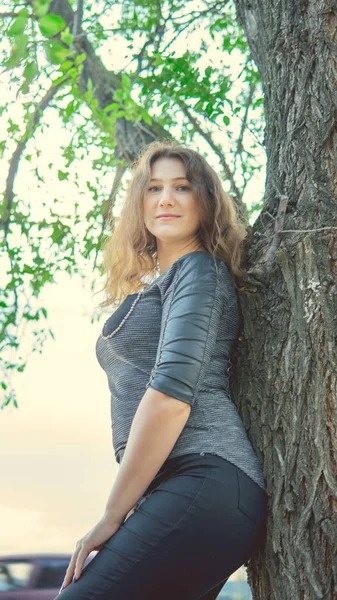 Hermosa mujer de pie cerca de un árbol y mirando a la cámara — Foto de Stock