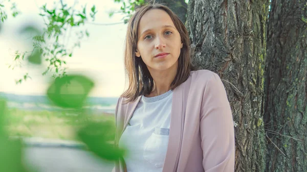 Ağacın yanında durup kameraya bakan güzel bir kadın.