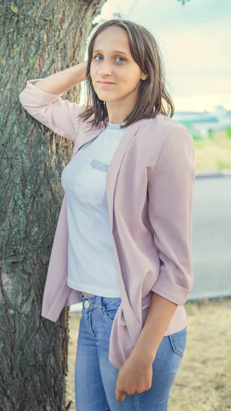 Mulher bonita de pé perto de uma árvore e olhando para a câmera — Fotografia de Stock