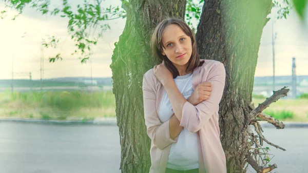 Bella donna in piedi vicino a un albero e guardando la fotocamera — Foto Stock