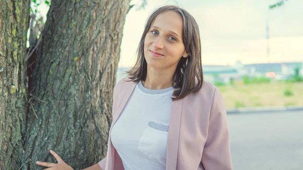 Hermosa mujer de pie cerca de un árbol y mirando a la cámara — Foto de Stock