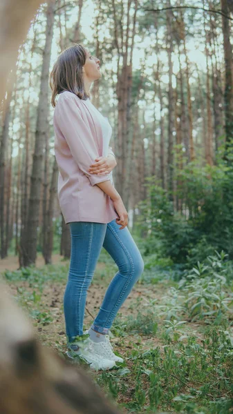 Vékony fiatal nő a zöld erdőben. Fa gyűrű a fáról és figyelmes nő áll az erdőben, felnéz — Stock Fotó