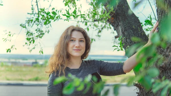 Женщина стоит возле дерева и смотрит в камеру — стоковое фото