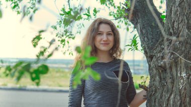 Ağacın yanında durup kameraya bakan güzel bir kadın.