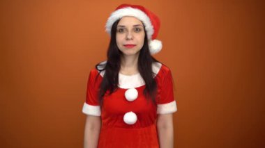 Noel Baba kostümüyle gülümseyen genç bir kadın turuncu arka planda hediyelerle dolu bir kutu tutuyor. Mutlu Noeller ve mutlu yıllar..