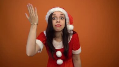 Noel Baba kostümüyle gülümseyen genç bir kadın turuncu arka planda hediyeler tutuyor. Mutlu Noeller ve mutlu yıllar..