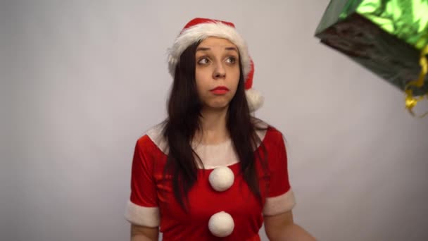 Lächelnde junge Frau im Weihnachtsmannanzug hält Geschenke auf weißem Hintergrund. Frohe Weihnachten und ein gutes neues Jahr. — Stockvideo
