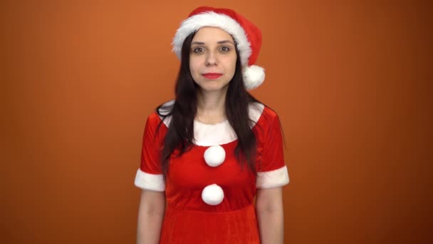 Eine lächelnde junge Frau im Weihnachtsmannanzug hält eine Schachtel mit Geschenken auf orangefarbenem Hintergrund. Frohe Weihnachten und ein gutes neues Jahr. — Stockvideo