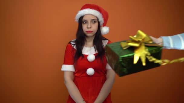 Lächelnde junge Frau im Weihnachtsmannanzug hält Geschenke auf orangefarbenem Hintergrund. Frohe Weihnachten und ein gutes neues Jahr. — Stockvideo