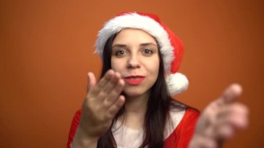 Noel Baba kostümü içinde gülümseyen genç bir kadın turuncu arka plandaki kameraya bakıyor. Mutlu Noeller ve mutlu yıllar..