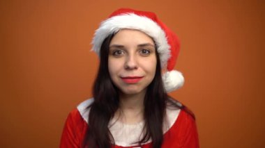 Noel Baba kostümü içinde gülümseyen genç bir kadın turuncu arka plandaki kameraya bakıyor. Mutlu Noeller ve mutlu yıllar..