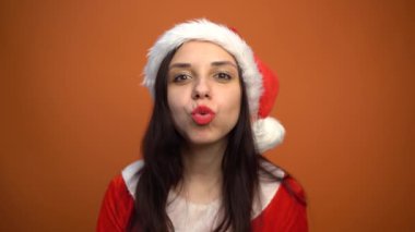 Noel Baba kostümü içinde gülümseyen genç bir kadın turuncu arka plandaki kameraya bakıyor. Mutlu Noeller ve mutlu yıllar..