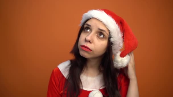 Leende vacker ung kvinna i Santa Claus kostym tittar på kameran på en orange bakgrund. God Jul och Gott Nytt År. — Stockvideo