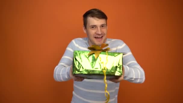 Szomorú jóképű férfi kapott egy ajándékot, és elkezdett boldogan táncolni egy narancssárga háttér. Üdülési koncepció, üdülési kedvezmények, ajándékok és eladások. — Stock videók