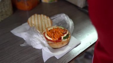 Mutfakta çizburger ve hamburger hazırlayan bir kadın. Masanın üzerinde malzemeler var. Şef hamburger hazırlar, fast food pişirir.