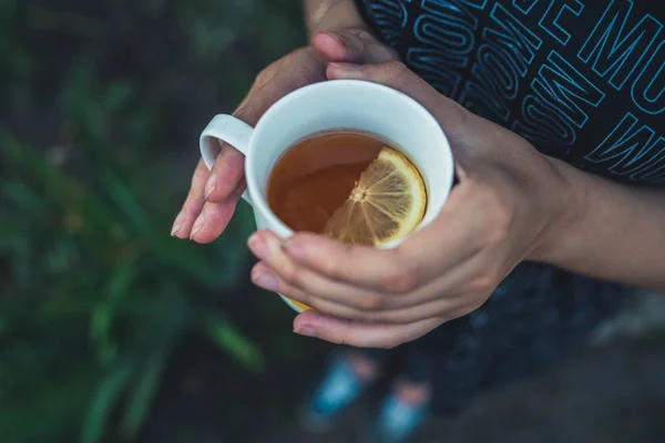 Gadis itu memegang secangkir teh dengan lemon. Perempuan dalam teh musim panas dingin minum teh di jalan. — Stok Foto