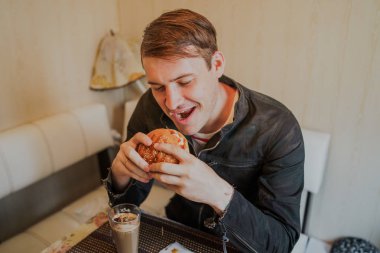 Mutlu adam fast food yiyor, hamburger. Bir adam masada oturuyor ve çizburger yiyor.