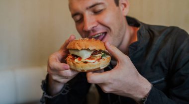 Mutlu adam fast food yiyor, hamburger. Bir adam masada oturuyor ve çizburger yiyor.